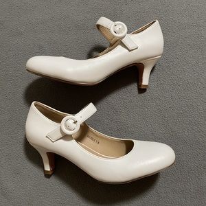 Short 50’s style white heels with a small circular buckle.